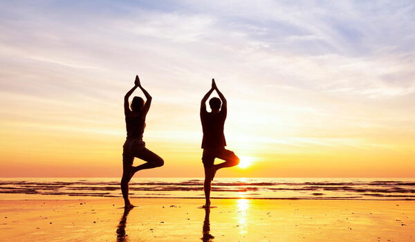 Paar übt Yoga am Strand im Sonnenuntergang Gegenlicht