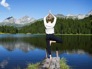 Frau von hinten fotografiert übt Yoga am Bergsee mit Alpenpanorama