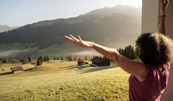 Frau von hinten mit ausgestreckten Armen in einer Yoga-Haltung vor weitem Tal in der Schweiz