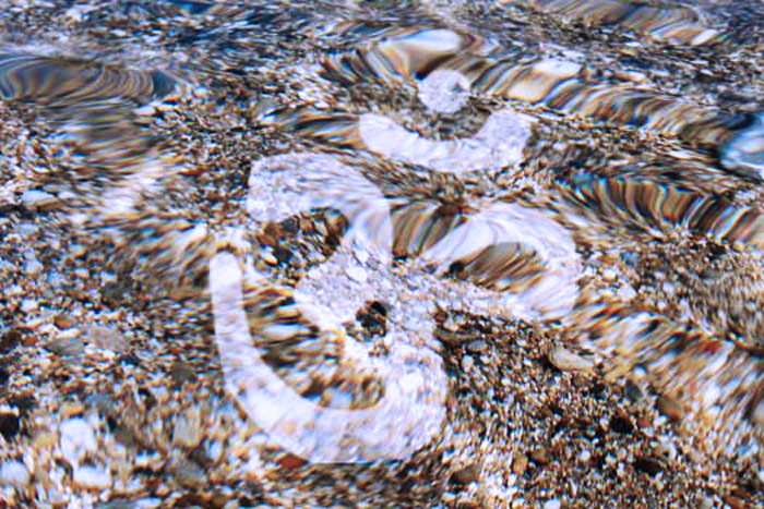 Om Zeichen auf transparenter Wasseroberfläche mit Kiesuntergrund